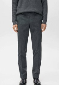 Pantaloni grigi a righe sottili con una vestibilità su misura, realizzati in un tessuto testurizzato, dotati di tasche frontali e una cintura liscia. Scarpe nere completano il look.