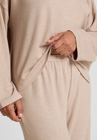 Beige loungewear set gemaakt van zachte stof, met een losse top met omslagmouwen en broek met elastische tailleband, met een gladde textuur.
