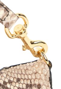 Fermoir doré reliant une sangle beige à texture peau de serpent à un coin de sac assorti avec un bord noir sur fond blanc.