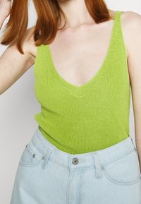 Stickad linne i ljus limegrön med djup V-ringning och smala axelremmar, parat med ljusa denimshorts med framknäppning.