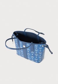 Sac fourre-tout bleu en toile à motifs avec des accents en cuir. Dispose de deux poignées, d'une ouverture sur le dessus et d'une poche intérieure. Forme ovale.