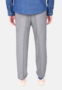 Pantaloni grigi su misura con una texture liscia, caratterizzati da pieghe a scatola. Indossati con sneaker bianche e accenti blu visibili sulle caviglie, provenienti da una camicia di jeans.