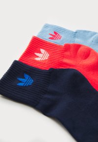 Drie paar sokken: marineblauw met blauw logo, koraal met rood logo en lichtblauw met roze logo. Allemaal met ribbeltextuur en onderscheidende logo's.