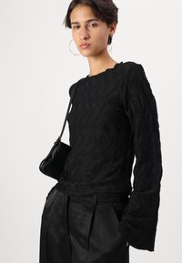 Top nero a maniche lunghe con tessuto testurizzato e motivo, colletto a scallop, abbinato a pantaloni neri a vita alta e una borsa a tracolla piccola.