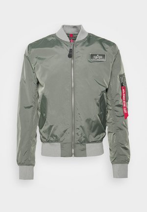 Giacca bomber verde oliva in nylon lucido, con chiusura a zip frontale, polsini a costine, tasche laterali e un'etichetta in tessuto rossa sulla manica.