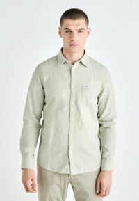 Light green long-sleeve shirt made of textured fabric. Features a button-down collar and a chest pocket with a small brand label.