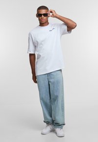 White cotton t-shirt with non-graphic text, light blue wide-leg jeans, and black sunglasses; footwear is white sneakers.