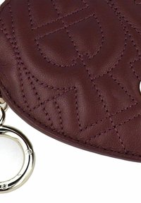 Pochette en cuir grenat avec un design matelassé. Elle est dotée de ferrures de couleur argentée et d'un anneau porte-clés circulaire. Texture lisse et coutures nettes.