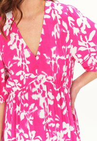 Rotes Kleid mit einem weißen Blumenmuster, V-Ausschnitt-Design, kurzen Puffärmeln und gerafftem Taillenbund. Weicher Stoff mit fließender Silhouette.