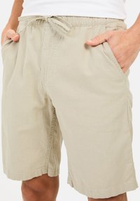 Lys beige shorts lavet af blødt stof med elastisk talje, bindelukning og sidelommer. Har en afslappet pasform og lige kant.