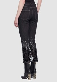 Jeans in denim nero con la metà inferiore decorata da paillettes, creando un effetto sfumato. Il taglio è diritto con due tasche posteriori visibili.