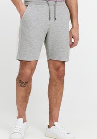 Shorts en coton gris avec une taille élastique et un cordon de serrage, dotés de poches latérales et d'une coupe au genou. Baskets blanches aux pieds.