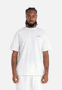 Witte katoenen t-shirt met korte mouwen, ronde hals en klein blauw geborduurd logo op de borst. Heeft een relaxte, boxy pasvorm.