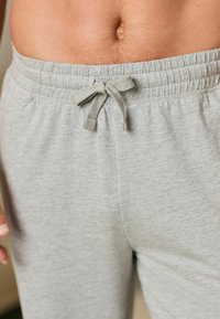 Graue Baumwoll-Sweatpants mit einem elastischen Taillenbund, Kordelzug und einer weichen, strukturierten Oberfläche. Sichtbare Hand in der Nähe des Taillenbundes.