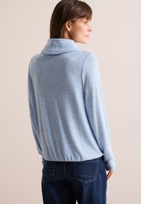 Helles blaues, weiches, langärmliges Pullover mit Schlupfkragen, lockerer Passform und gerippten Bündchen, kombiniert mit dunklen Jeans.