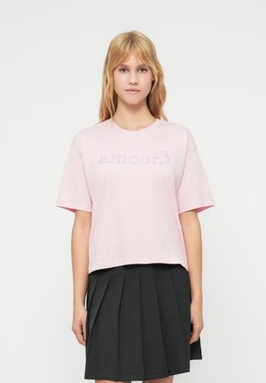 Lyserød t-shirt med korte ærmer og afslappet pasform med teksten "amour" i rhinsten på forsiden. Bæres med et plisseret sort nederdel.