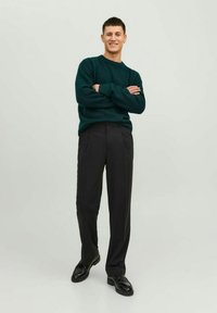 Pull en maille texturée vert avec col ras du cou, associé à un pantalon plissé noir et des chaussures noires, offrant un look décontracté.