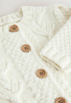 Gilet en tricot crème avec des motifs texturés, doté de boutons en bois et d'un col à rabat. Matière douce et épaisse, idéale pour le superposition.