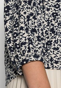 Top azul-marinho com padrão floral e mangas franzidas, apresentando uma textura suave e um decote arredondado, enfatizando um design casual.