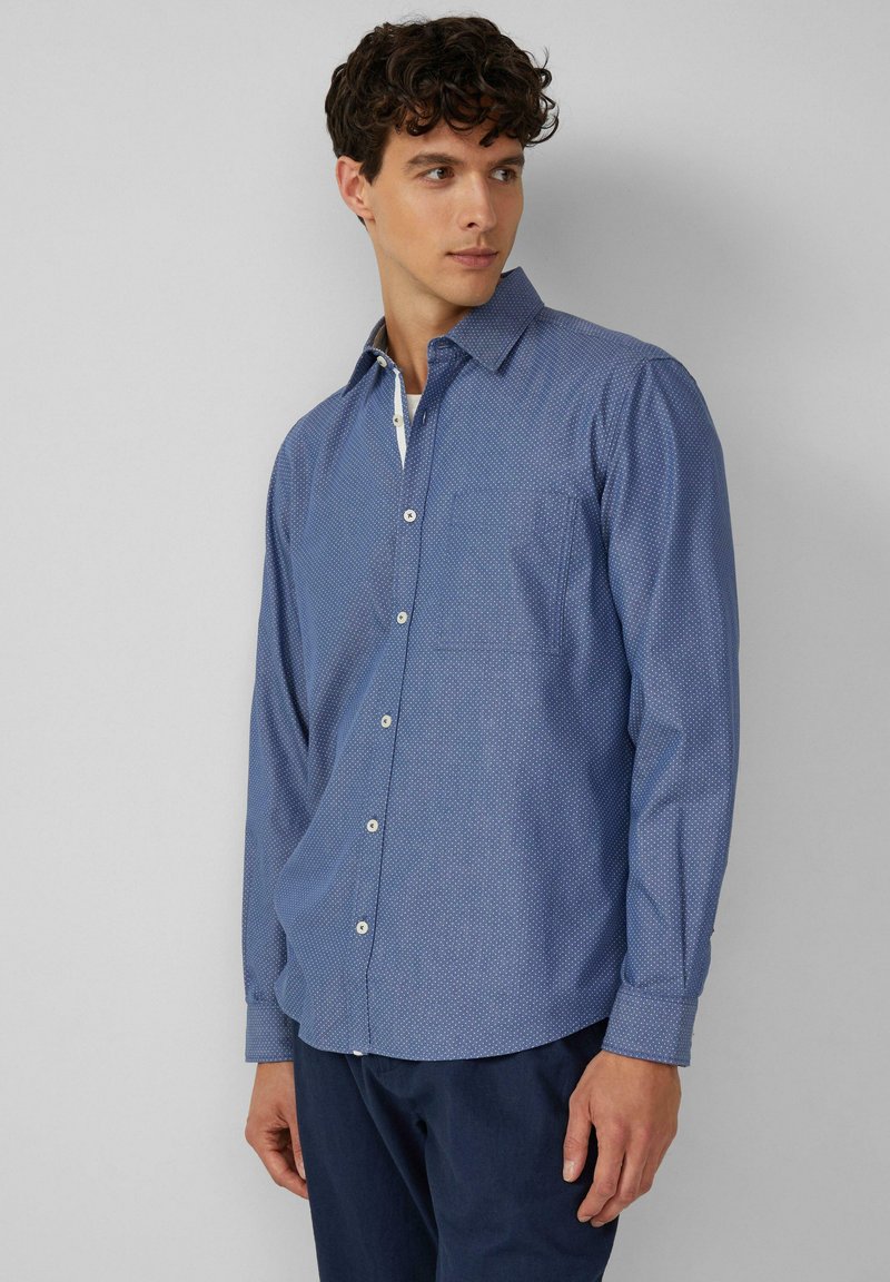 Camisa de hombre con botones en un tejido azul claro con estampado, con collar, un bolsillo en el pecho y botones blancos. Mangas largas y dobladillo curvado.