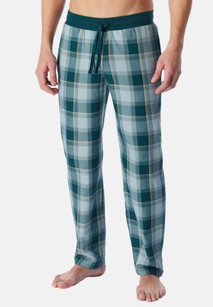 Man wearing green and blue plaid pajama pants with a dark green elastic waistband and drawstring, standing barefoot on a white background.