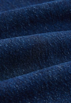 Sötétkék farmeranyagon finom textúrával, látható varrásokkal és enyhe fényességgel, lágyított redők és eltérő árnyalatokkal.