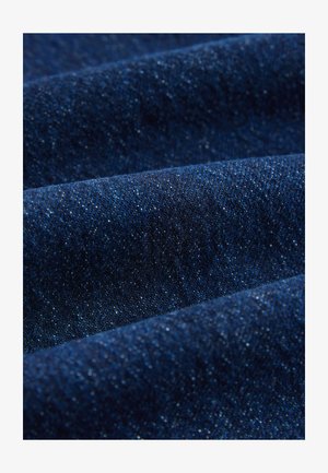 Tessuto in denim blu scuro con una trama sottile, caratterizzato da cuciture visibili e una leggera lucentezza, che mette in mostra pieghe ammorbidite e tonalità variabili.