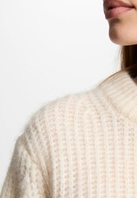 Maglione crema strutturato con motivo a coste e un ampio colletto, che mette in risalto un materiale morbido e peloso.