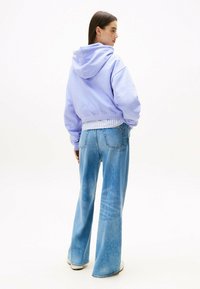 Felpa con cappuccio lavanda e fondo a coste, abbinata a jeans svasati azzurri chiari. Tessuto morbido, vestibilità comoda e dettagli di cucitura sottili.