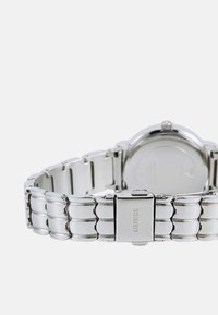 Silberne Metallarmbanduhr mit einem glatten, verlinkten Armband und einem runden Gehäuse. Verfügt über ein schlichtes Zifferblatt und eine Verschluss mit "GUESS"-Markierung.