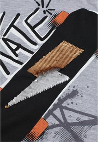 Grijze stof met een grafisch ontwerp in zwart, wit en oranje. Pailletten in zilveren en koperen vormen, wat textuur en contrast toevoegt.