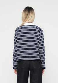 Mørkeblå og hvit stripete langermet skjorte med rund hals og en kontrasterende hvit krage, laget av et mykt, teksturert stoff.