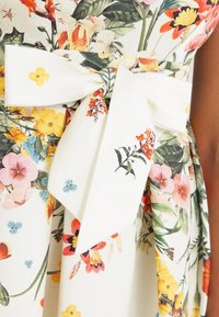 Blommig klänning med vit bakgrund, med färgglada blommönster, ett bågskärp i midjan och en svävande kjol.