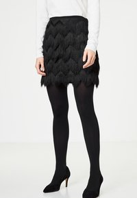 Svart kjol med texturerade, lager-på-lager fransar i ett chevronmönster. Bärs med svarta leggings och klackar; har en fitted midja.