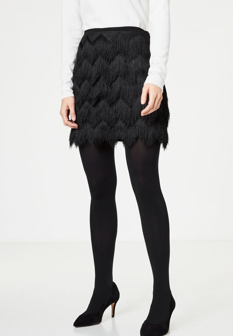 Svart kjol med texturerade, lager-på-lager fransar i ett chevronmönster. Bärs med svarta leggings och klackar; har en fitted midja.