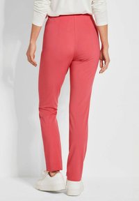 Rosa, figurbetonte Hose mit hoher Taille und eingeprägten Details, kombiniert mit weißen Sneakers, von hinten gezeigt. Glatte Textur und leichtes Material.