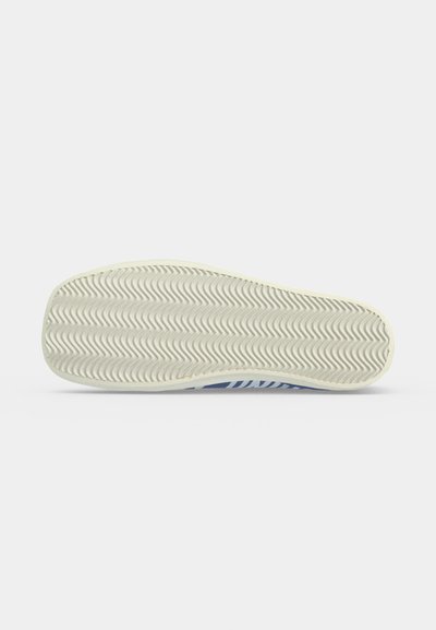 Semelle de chaussure avec motif de bande de roulement en zigzag texturé en gris clair, présentée à plat sur un fond blanc uni.