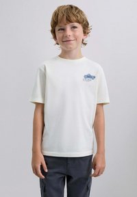 Camiseta blanca de manga corta con un gráfico azul de un camión vintage en la parte izquierda del pecho. Hecha de suave tela de algodón.