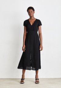 Black, short-sleeve dress featuring a V-neck, fitted waist, and a front slit. Fabric appears lightweight with a flowing silhouette.