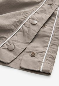Tissu marron clair avec une texture lisse, comportant de grands boutons ronds et des coutures blanches contrastantes le long des bords.