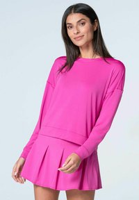 Rosa Langarmtop mit rundem Ausschnitt und lockerer Passform, kombiniert mit einem plissierten rosa Rock, beide aus einem glatten, dehnbaren Stoff gefertigt.