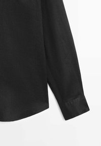 Manica e lato inferiore di una maglia nera a manica lunga con polsino, esposti su sfondo bianco.