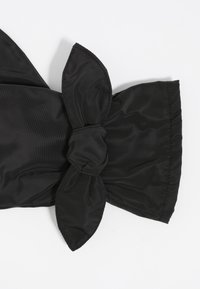 Lazo negro hecho de tela lisa y texturizada, con un nudo central y dos extremos puntiagudos. Los bordes están cuidadosamente cosidos, lo que mejora la durabilidad.