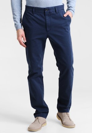 Chinos en coton bleu marine avec une coupe droite, poches avant et une texture subtile ; associés à des chaussures à lacets beige clair.