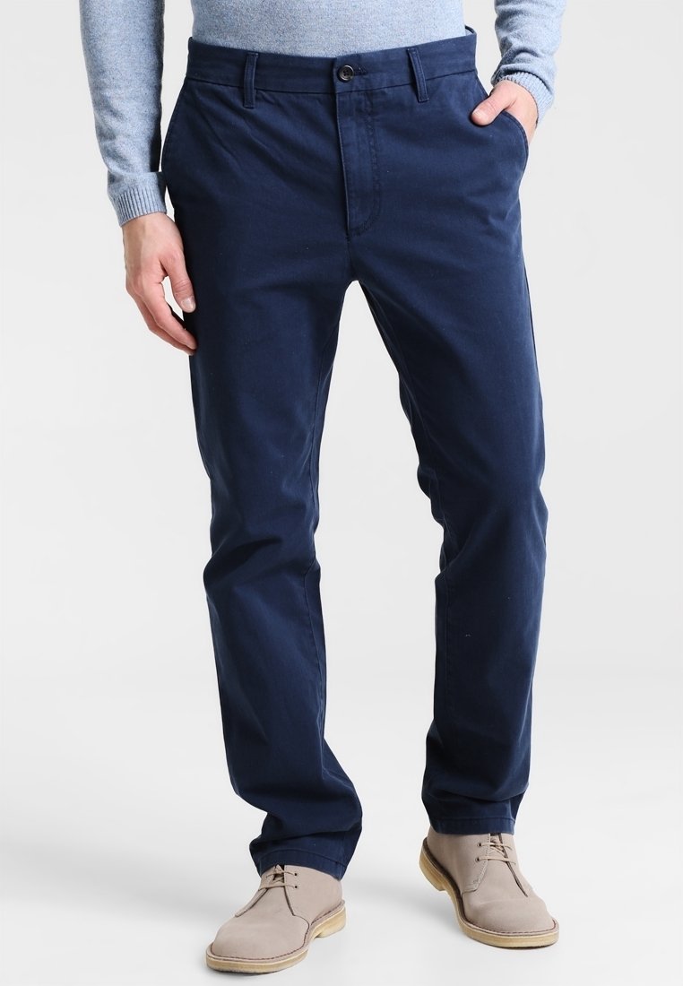 Navy blue cotton chinos with a straight-leg design, front pockets, and a subtle texture; paired with light beige lace-up shoes.