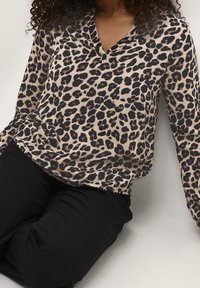 Blusa con stampa leopardata, scollo a V profondo, maniche lunghe e tessuto morbido e leggero. Abbinata a pantaloni neri.