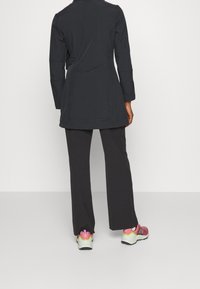 Chaqueta negra, ligera y de manga larga con un corte ajustado y cuello estructurado, combinada con pantalones negros holgados y zapatillas deportivas multicolores.