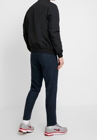 Czarna kurtka bomberka z prążkowanymi mankietami, zestawiona z ciemnoniebieskimi, dopasowanymi spodniami. Srebrne trampki z czerwonymi akcentami dopełniają strój.