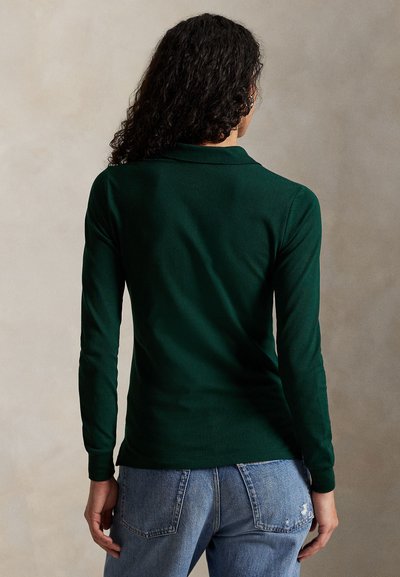 Ciemnozielona, długorękawowa koszulka polo z kołnierzykiem. Charakteryzuje się dopasowanym krojem i gładką fakturą, noszona z jasnoniebieskimi, postarzanymi dżinsami.