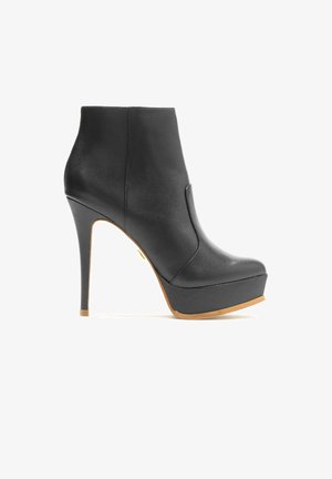 Zwarte leren enkelboot met een hoge stilettohak en platform. Kenmerkt zich door een gladde textuur en een subtiele uitsnijding aan de zijkant.